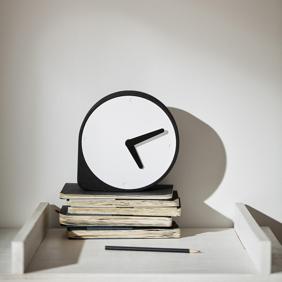 A Puik Clork Table Clock, Black, with an asymmetrical shape, sits on top of a stack of books.