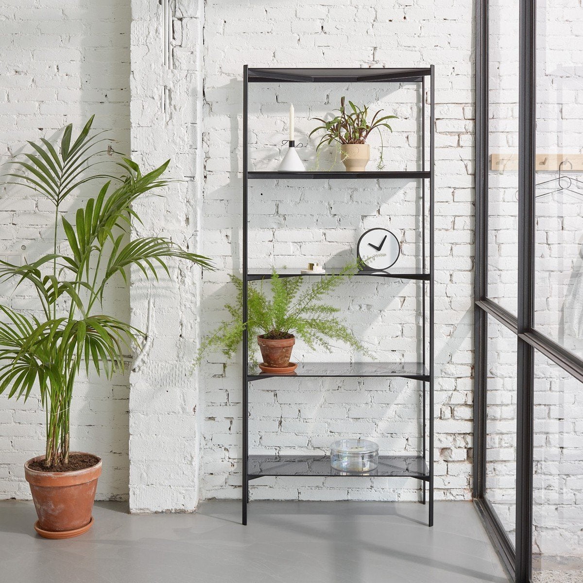 A black shelf with a potted plant in front of a white wall. The black shelf features an asymmetrical shape, complemented by the presence of a Puik Clork Table Clock.